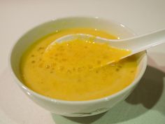 a white bowl filled with yellow liquid and a spoon in the bowl next to it