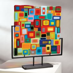 a colorful art piece is displayed on a white surface with a black stand holding it