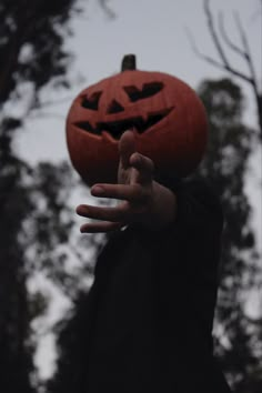 a person in a black jacket is holding up a jack - o'- lantern