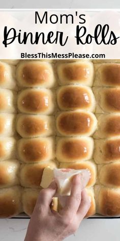 a person holding a piece of bread in front of a pan with rolls on it