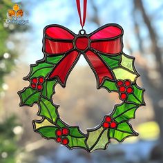 a stained glass christmas wreath ornament hanging from a window with a red ribbon