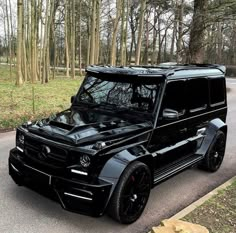 a black mercedes g - class is parked on the side of the road in front of some trees