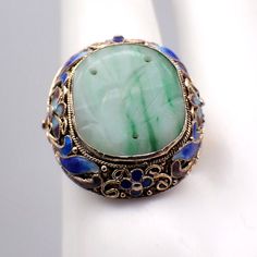 Vintage Chinese silver ring in floral filigree designs with vermeil finish and colorful enamel decorations, featuring carved oval green Jade centerpiece. The size is adjustable. This gorgeous ring is a size 7 1/4 (adjustable), 24 mm at the widest and weighs 6.5 grams. It features some enamel loss. EA2362 Green Oval Enamel Ring With Gemstone, Green Oval Enamel Ring For Formal Occasions, Oval Green Enamel Ring With Gemstone, Formal Green Oval Enamel Ring, Formal Oval Green Enamel Ring, Oval Green Enamel Ring Gift, Green Cabochon Enamel Jewelry, Green Enamel Ring For Wedding, Green Enamel Jewelry For Wedding