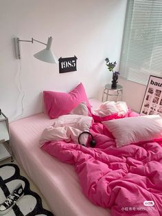 a bed with pink sheets and pillows in a white room next to a black and white rug