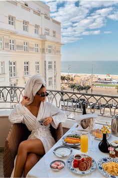 a woman sitting at a table with food and drinks on it in front of the ocean