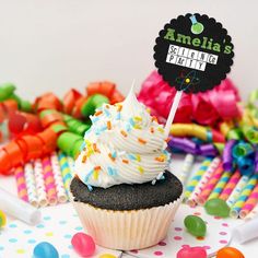 a cupcake with white frosting and sprinkles sits on a table surrounded by candy