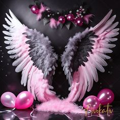 two large white and black wings with pink balloons on the floor in front of a dark background