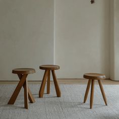 three wooden stools sitting next to each other on a carpeted floor in front of a white wall