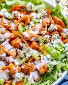 a salad with chicken, cheese and lettuce in a white bowl on a blue cloth