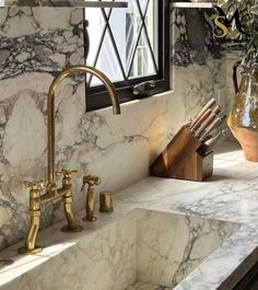 a marble sink with gold faucets and wooden utensils in front of a window