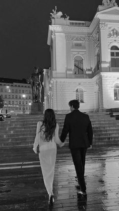 a man and woman holding hands walking down the street in front of a building at night