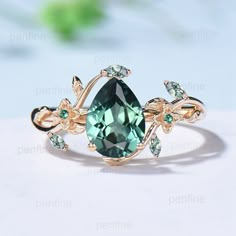 a ring with an oval green stone surrounded by leaves and diamonds on a white surface