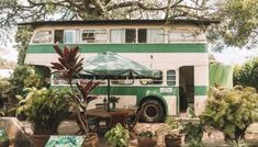 a green and white double decker bus parked in front of a table with an umbrella