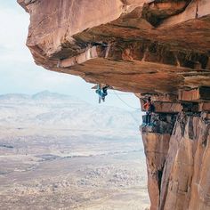 a man climbing up the side of a cliff with a rope attached to his feet