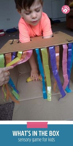 a young child is playing in a box with streamers on the floor and an adult's hand reaching for it