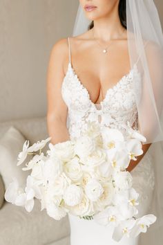 a woman in a wedding dress holding a bouquet of white flowers and wearing a veil