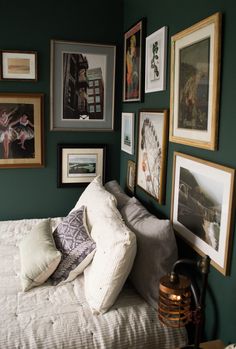 a bedroom with green walls and pictures on the wall above the bed, along with other framed art