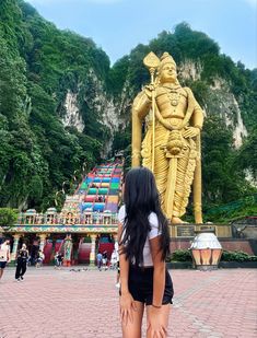 a woman standing in front of a golden statue on the side of a mountain with trees