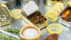 several tins filled with food sitting on top of a counter next to lemon slices