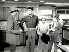 an old black and white photo of people standing in a kitchen with one man wearing a hat