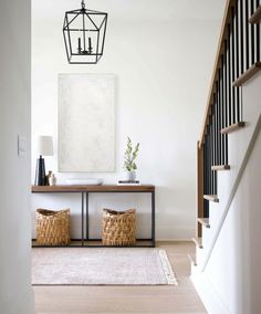 a hallway with white walls and wooden floors, two baskets on the floor, an art piece hanging from the ceiling