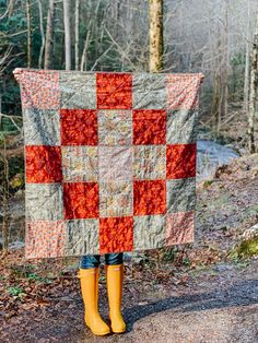 a woman in yellow rubber boots holding up a quilt