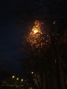 a street light shines brightly in the night sky above parked cars on a city street