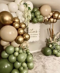 balloons and greenery are arranged in the corner of a room with white, gold and green decorations