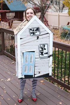 a woman in striped socks holding up a house made out of cardboard with windows and doors