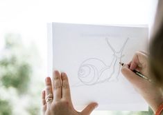 a woman is drawing a snail on a piece of paper