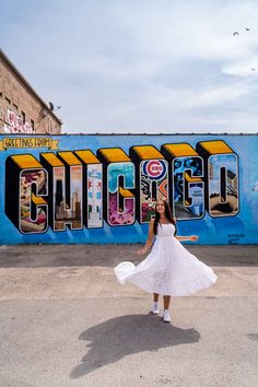 a woman in a white dress is standing in front of a wall with the word chicago painted on it