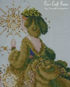 a cross - stitch picture of a woman in a green dress with snowflakes on her head