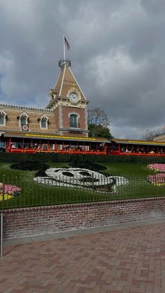 a building with a clock in the center and flowers on the front lawn behind it