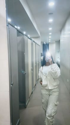 a woman in white is walking down the hallway with her cell phone up to her ear