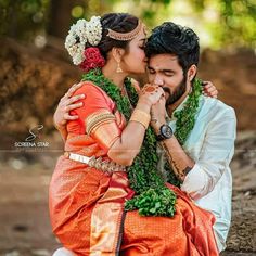 a man and woman sitting next to each other in front of some trees with flowers on their heads