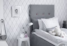 a teddy bear sitting on top of a bed in a room with white and gray walls