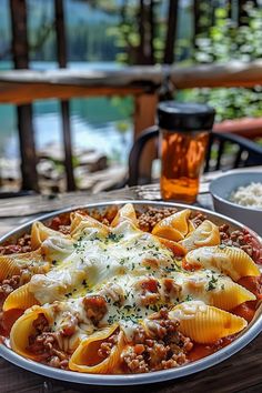 a plate of pasta with meat and cheese on a wooden table next to a glass of beer