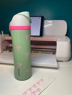 a green and pink water bottle sitting on top of a white table next to a printer