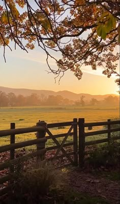 the sun is setting over an open field with a fence in front of it and mountains in the distance