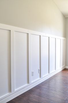 an empty room with white paneling and wood floors