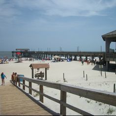 people are walking on the beach near a pier