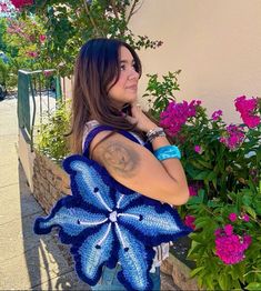 a woman holding a blue crocheted bag next to flowers