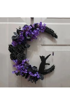 a black cat sitting on top of a purple and black wreath with flowers around it