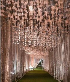 the walkway is lined with crystal beads and draped in white sheer curtains, along with lush green grass