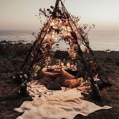 a teepee is set up with lights and blankets on the grass near the ocean