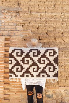 a person standing in front of a brick wall holding a brown and white blanket over their head