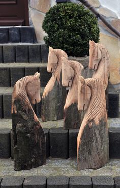 four carved wooden horses on steps in front of a building with stairs leading up to the door