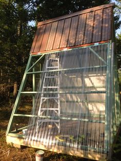 a small green house in the woods with a ladder up to it's roof