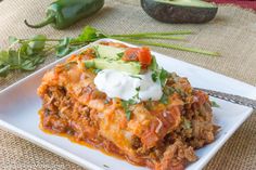 an enchilada casserole with sour cream on top sits on a white plate