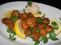 a white plate topped with fried food next to lemon wedges and garnish